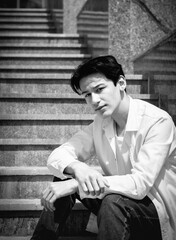 Young man, teenage model sits on steps in city. Casual, fashion. BW grainy photo