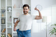 © Liubomir - Portrait of a happy and confident young man at home, showing his weight and waist in oversize jeans, showing a sit and victory gesture with his hand.