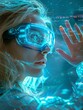 © Business Pics - an attractive blonde young woman with futuristic head-up glasses, hand outstretched, she is working on the future, blue tech Background