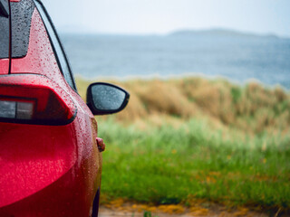 Wall Mural - a red car is parked on the side of a road next to a grassy field with tall grass on a dune and ocean