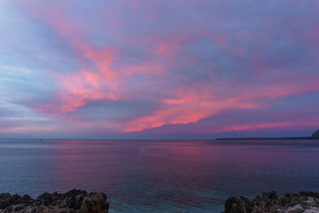 Coast with turquoise water at Nature Park of Monte Cofano during evening twilight with red illuminated clouds, San Vito Lo Capo, Sicily, Italy