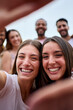 © CarlosBarquero - Vertical. Close up two girl friends making frame with hands. Unfocused group of young people is happily celebrating, taking a selfie together. Smiling women having fun during their leisure travel