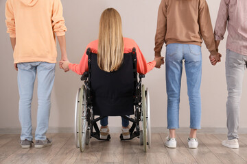 Wall Mural - Group of teenagers with girl in wheelchair holding hands near light wall, back view