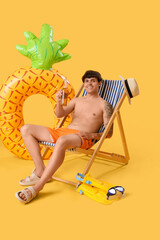 Canvas Print - Young man with beer in deck chair on yellow background