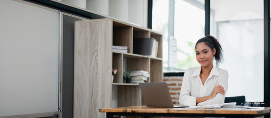 Wall Mural - Professional woman in white shirt working on a laptop in a contemporary office setting with bookshelves and large windows.