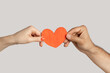 © khosrork - Closeup of multicultural woman and man hands holding together red paper heart, symbol of love. Indoor studio shot isolated on gray background.