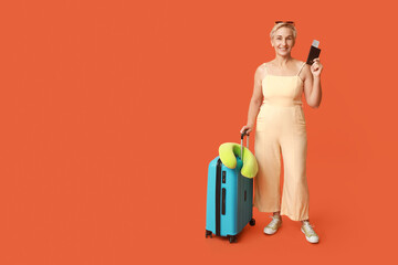 Mature female traveler with passport and suitcase on orange background