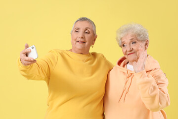 Poster - Senior female friends taking selfie on yellow background