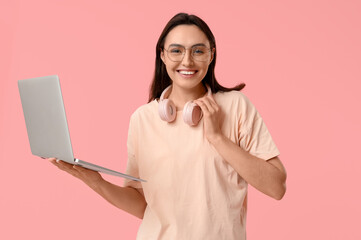 Wall Mural - Pretty young woman with laptop and headphones on pink background