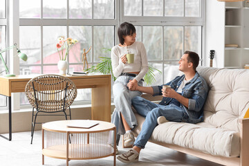 Wall Mural - Young couple in love with cups of coffee chatting at home