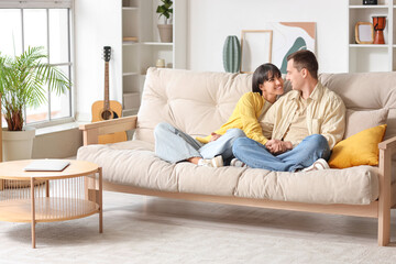 Wall Mural - Young couple in love hugging on sofa at home