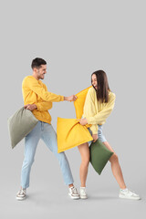 Poster - Young couple fighting pillows on light background