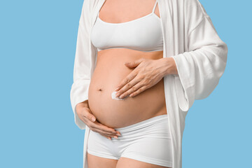 Poster - Young pregnant woman applying cream against stretch marks on blue background