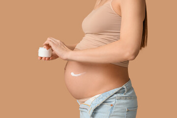 Wall Mural - Young pregnant woman with cream against stretch marks against beige background