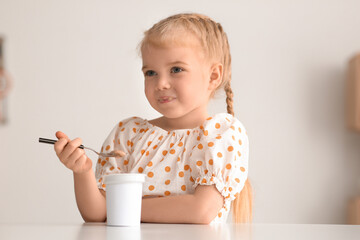 Wall Mural - Cute little girl with spoon eating yogurt at home