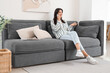 © Pixel-Shot - Young woman talking with mobile phone on black sofa in living room
