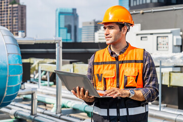 Portrait of caucasian engineer man in uniform holding laptop computer and working in at plumbing and electrical systems on the roof of a building