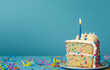 © Mirador - Slice of colorful birthday cake with a lit candle on a blue background, perfect for birthday celebrations and festive occasions.