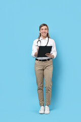 Canvas Print - Portrait of happy doctor with stethoscope and clipboard on light blue background