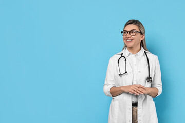 Canvas Print - Portrait of happy doctor with stethoscope on light blue background, space for text