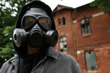 Wall Mural - Man in gas mask near building outdoors, low angle view. Space for text
