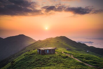 Sticker - mountain cabin sitting on top of grassy hill under beautiful sunset