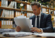 © Holly Berridge - A businessman holding paperwork in an office, showcasing professionalism, organization, and corporate environment.