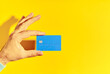 © GVS - Male hand holds blue plastic bank card over yellow background with copy space