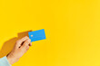 © GVS - Male hand holds blue plastic bank card over yellow background with copy space