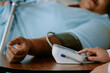 © AnnaStills - Close up photo of nurse pushing button of tonometer on top of table while senior African American patient lying with tonometers cuff around her arm