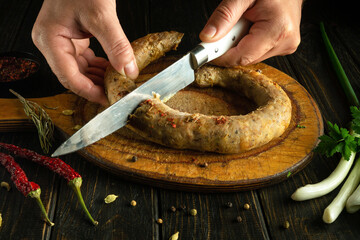 Wall Mural - A man slicing homemade sausage with a knife before serving it on a festive table.