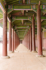 a long corridor with traditional Korean architecture, featuring colorful wooden beams and a series of red pillars leading to a vanishing point.