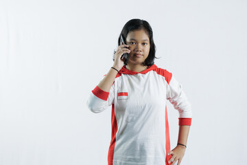 a young Indonesian woman is on the phone with her cell phone and looks happy, concept of Indonesia's independence day on August 17, isolated on a white background