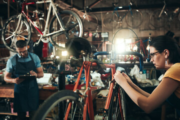 People, bicycle mechanic and fix with inspection for maintenance or small business at repair shop together. Young man, woman or cycling engineers working on bike with tools or equipment at workshop