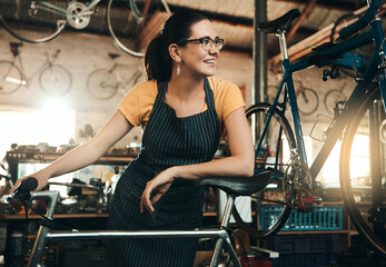 Workshop, woman and bicycle repair shop with mechanic, technician or maintenance with apron. Happy, service smile and business owner with startup, pride or bike for fixing with entrepreneur in garage