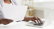 © Prostock-studio - Cropped of professional black woman is handling documents at her desk in an office. The setting is sleek and organized, with a clean desk, contemporary decor