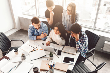 Aufkleber - A diverse group of individuals, both men and women, are seated around a table. They are focused on a laptop in the center, engaged in a discussion or meeting, high angle view