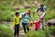 © Marko Geber - Happy family hiking by a stream with children carrying teddy bear
