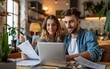 © neirfy - A young couple working on their financial goals for their dream home The man and woman working together on a laptop at a table in a modern apartment interior,.
