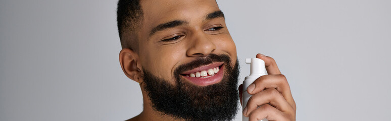 Wall Mural - Young african american man with a beard holding a tube of locion.