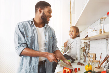 Wall Mural - Cute little afro girl and her dad cooking in kitchen at home