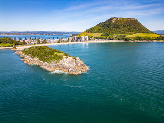 Wall Mural - drone shot of mount maunganui beachfront, capturing rocky peninsular, holiday homes and bush covered