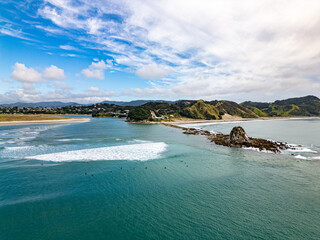 Wall Mural - aerial view of surfers waiting for waves in prime spot by rocky peninsular in mangawhai beach, new z