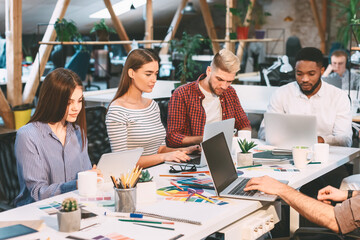 Poster - A group of young professionals work together in a modern, open-office environment with natural light, laptops, and design materials.