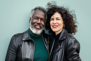 Wall Mural - Portrait of a glad multicultural couple in their 40s sporting a classic leather jacket while standing against pastel or soft colors background