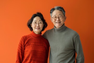 Portrait of a glad asian couple in their 60s wearing a classic turtleneck sweater in front of solid color backdrop