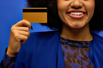 Stylish African American woman in trendy attire holding credit card, smiling.