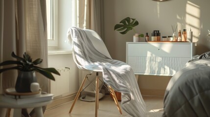 Poster - A white chair with a blanket draped over it sits next to a window in a bright bedroom. Natural light streams through the window, casting shadows on the floor and the white dresser.