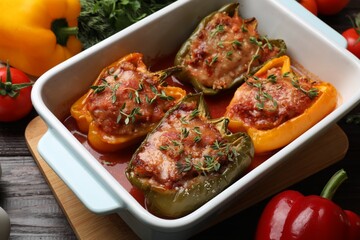 Wall Mural - Tasty stuffed peppers in dish and ingredients on wooden table, closeup