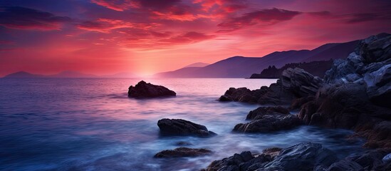 Wall Mural - Scenic view of the sun setting over the tranquil ocean, casting a warm glow on the rocks and water below. with copy space image. Place for adding text or design